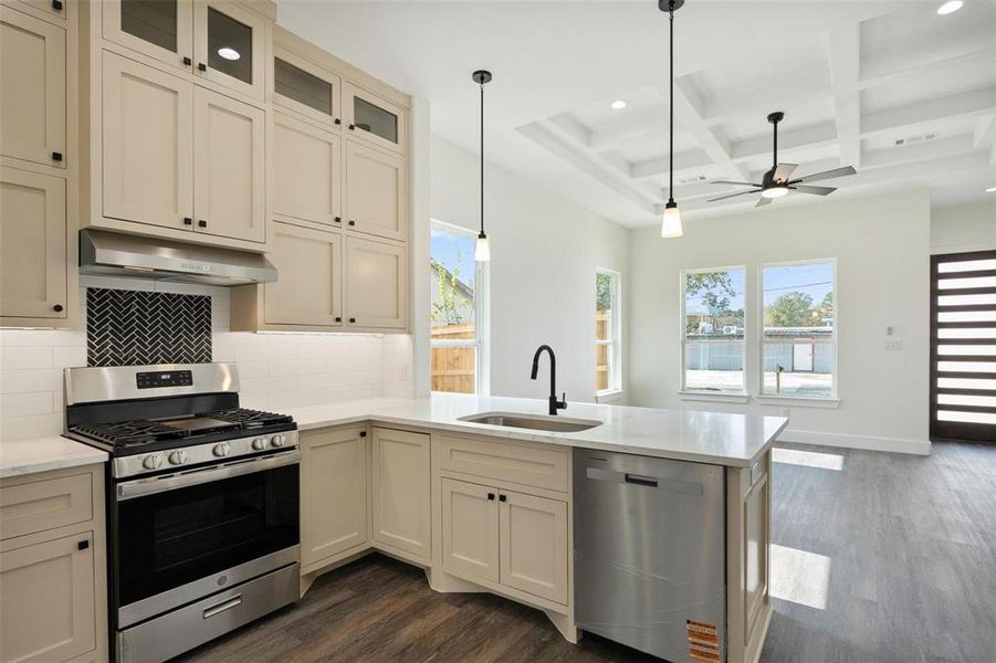 Kitchen with stainless steel appliances, cream cabinetry, coffered ceiling, backsplash, and dark wood-type flooring