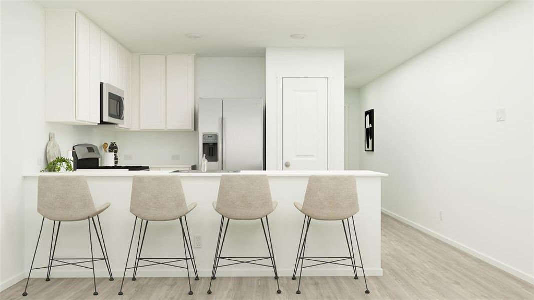 Kitchen with light wood-type flooring, white refrigerator with ice dispenser, range, a kitchen breakfast bar, and white cabinets