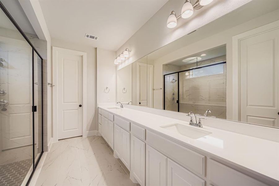 Bathroom with a marble finish shower, double vanity, and light marble finish floors