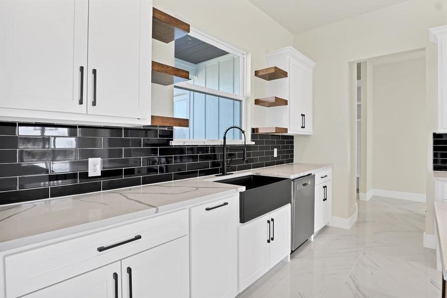 Kitchen with sink, white cabinetry, stainless steel dishwasher, light stone countertops, and decorative backsplash