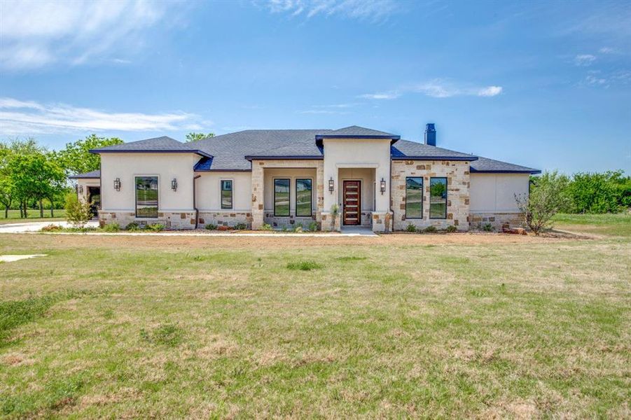 Prairie-style home with stucco siding, stone siding, and a front lawn