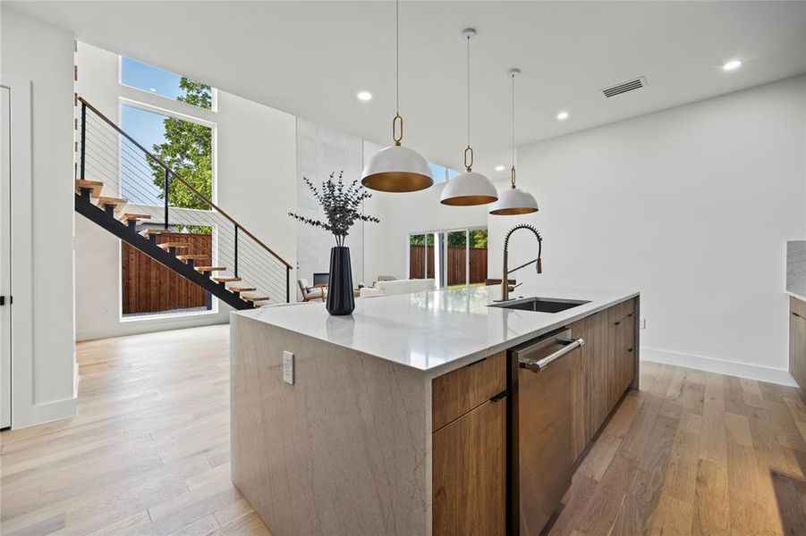 Kitchen featuring a kitchen island with sink, dishwasher, sink, light hardwood / wood-style flooring, and decorative light fixtures