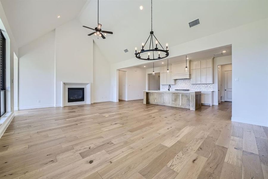 Unfurnished living room with ceiling fan with notable chandelier, light wood-type flooring, and high vaulted ceiling