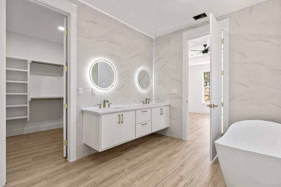 Full bathroom featuring double vanity, a walk in closet, light wood-type flooring, and a soaking tub