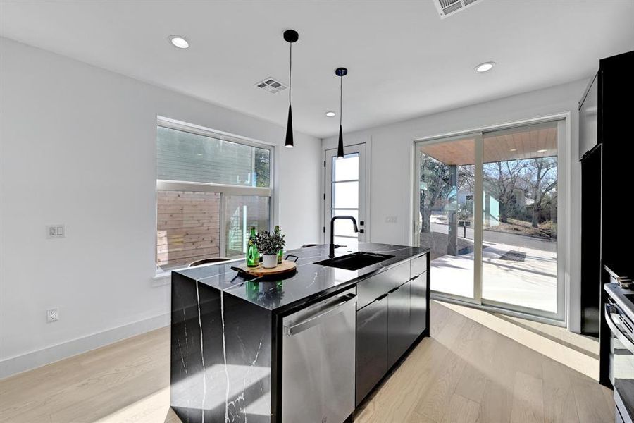 Kitchen featuring stainless steel appliances, a sink, dark cabinetry, light wood finished floors, and dark countertops