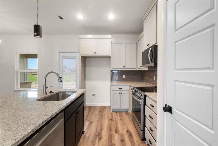 Kitchen with light stone countertops, stainless steel appliances, sink, decorative light fixtures, and white cabinetry Kitchen with light stone countertops, stainless steel appliances, sink, decorative light fixtures, and white cabinetry