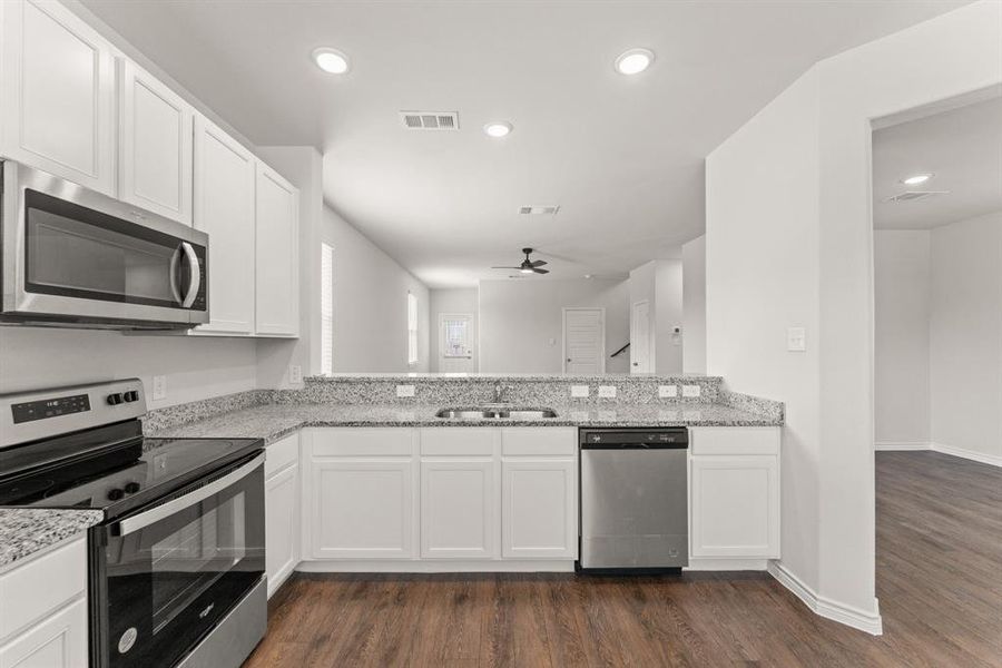 Kitchen with appliances with stainless steel finishes, white cabinetry, dark wood-style floors, light stone counters, and recessed lighting Kitchen with appliances with stainless steel finishes, white cabinetry, dark wood-style floors, light stone counters, and recessed lighting