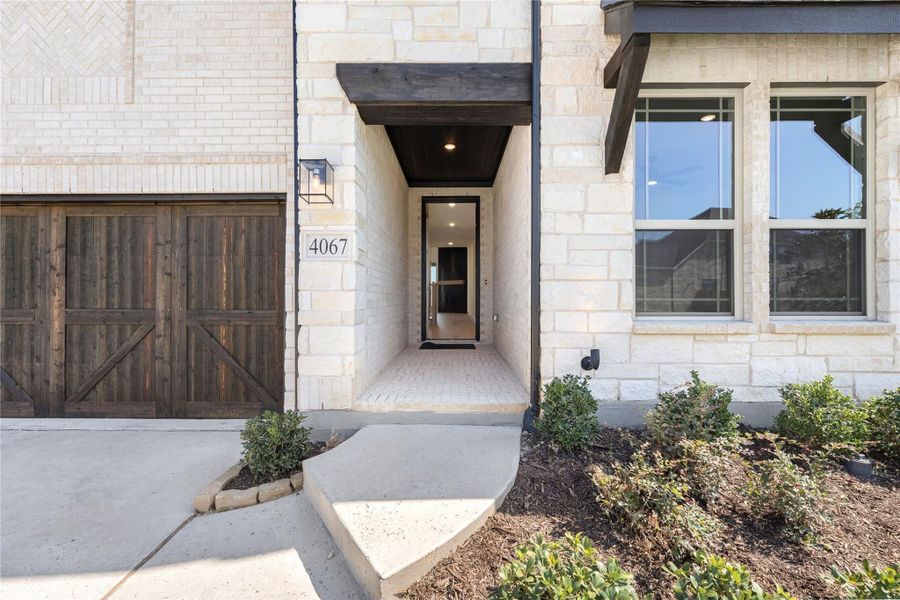 Home entrance with limestone exterior, covered entryway, wood garage door, and address number 4067.
