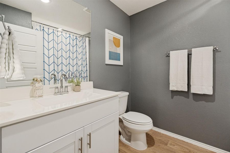 A well-appointed bathroom features a bright vanity with a modern sink, accompanied by warm wood-look flooring.
