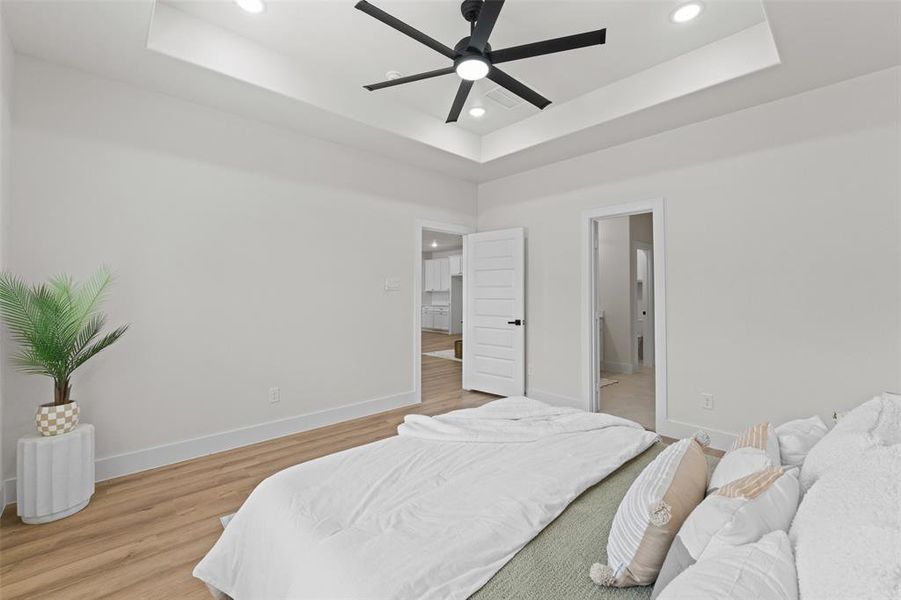 Bedroom featuring a tray ceiling, recessed lighting, light wood-type flooring, and baseboards Bedroom featuring a tray ceiling, recessed lighting, light wood-type flooring, and baseboards