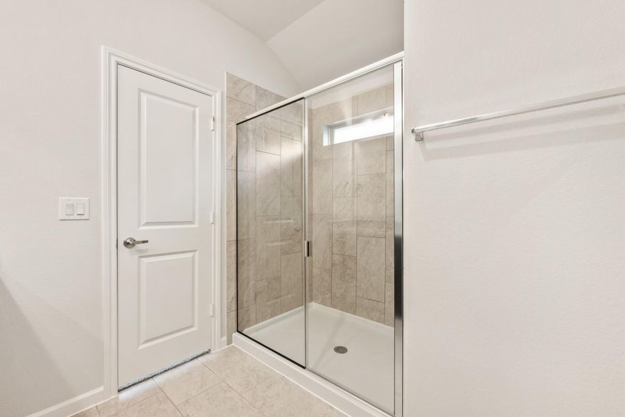 Walk-in shower with glass sliding doors and beige tile walls in a white bathroom Walk-in shower with glass sliding doors and beige tile walls in a white bathroom