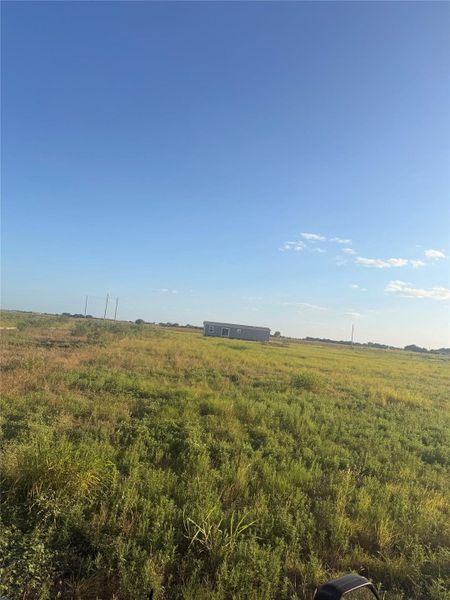 An open expanse of grassy acreage surrounds the property under a clear blue sky.