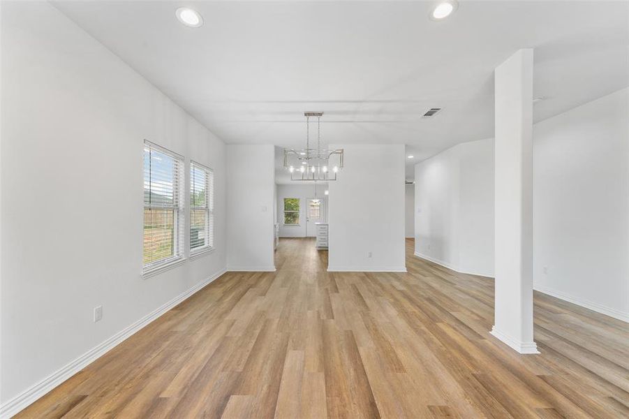 Open-concept living space featuring wood-finish flooring, recessed lighting, a contemporary chandelier, white walls, and multiple windows with blinds