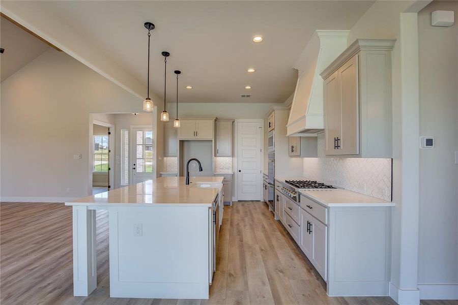 Kitchen with an island with sink, sink, tasteful backsplash, and light hardwood / wood-style flooring