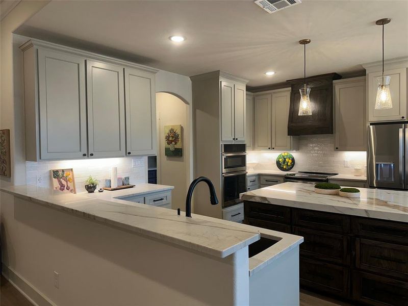 Contemporary kitchen featuring white cabinetry, light-toned countertops, a dark wood-finish island, built-in stainless steel appliances, and pendant lighting