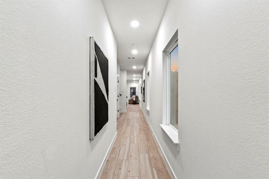 Hallway with recessed lighting, light wood-style floors, baseboards, and a textured wall Hallway with recessed lighting, light wood-style floors, baseboards, and a textured wall
