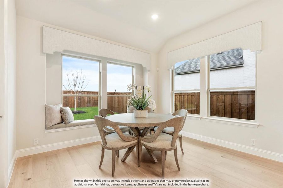 Bright breakfast nook with round wood table, four chairs, window seat, and hardwood floors