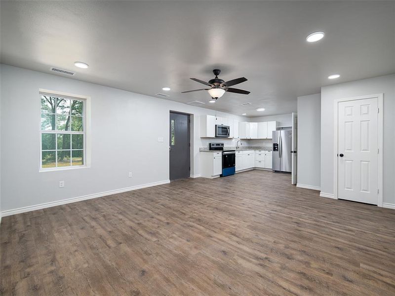 Kitchen with open floor plan, white cabinetry, stainless steel appliances, dark wood finished floors, and light countertops
