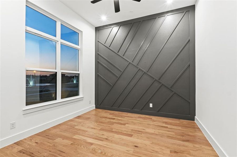 Empty room featuring baseboards, ceiling fan, light wood-type flooring, and a decorative wall