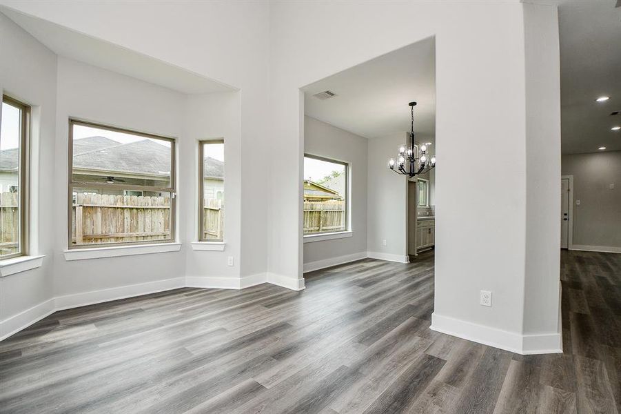 This is a spacious view of living and dinning rooms featuring elegant gray wood flooring, fresh white walls, ample natural light from large windows, and a stylish chandelier that adds a touch of sophistication. The open floor plan allows for versatile furnishing options.