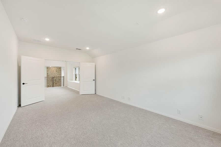 Empty bedroom with vaulted ceiling, light carpet, white walls, and two doors leading to hallway Empty bedroom with vaulted ceiling, light carpet, white walls, and two doors leading to hallway