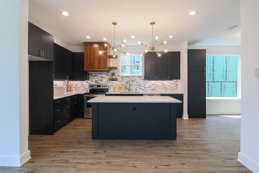 Kitchen with light hardwood / wood-style flooring, decorative light fixtures, stainless steel electric range oven, and a center island