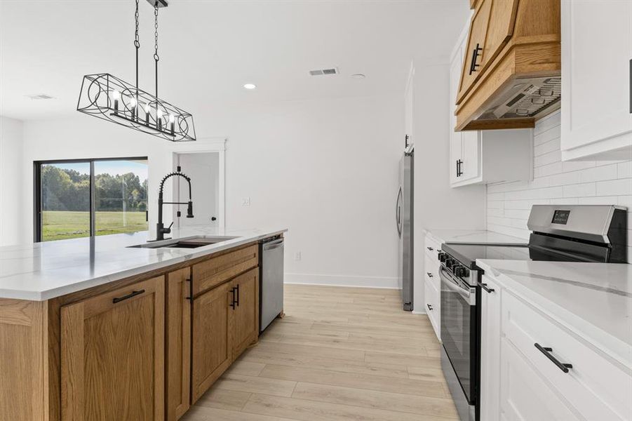 Kitchen with appliances with stainless steel finishes, hanging light fixtures, a kitchen island with sink, light wood-type flooring, and recessed lighting