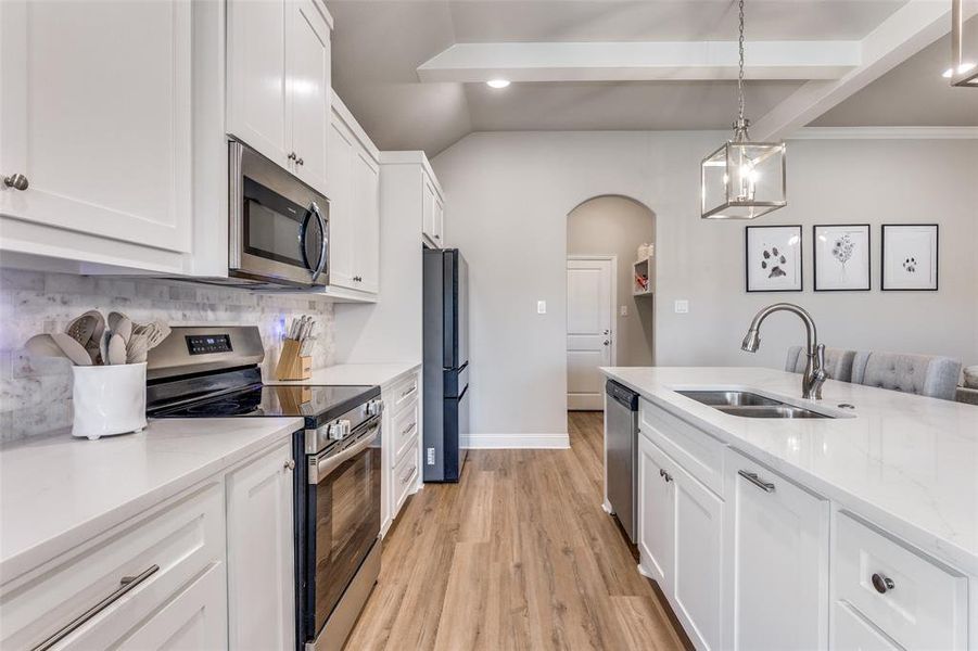 Kitchen with appliances with stainless steel finishes, arched walkways, light wood-type flooring, white cabinets, and light stone counters Kitchen with appliances with stainless steel finishes, arched walkways, light wood-type flooring, white cabinets, and light stone counters