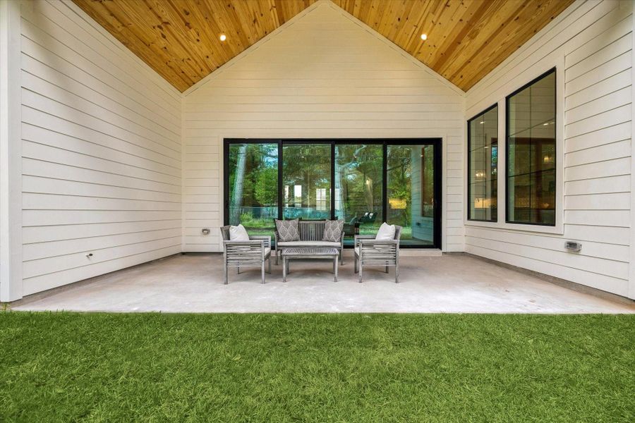 Covered outdoor living area with a vaulted wood ceiling, sliding glass doors, and open patio space.