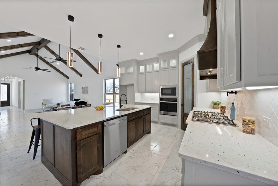 Kitchen featuring arched walkways, glass insert cabinets, open floor plan, light marble finish flooring, and light stone countertops