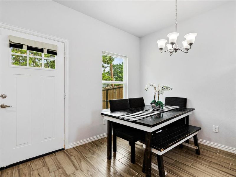 Bright dining area featuring a modern five-light chandelier, a white paneled door with glass inserts, a window offering natural light, and wood-finish flooring