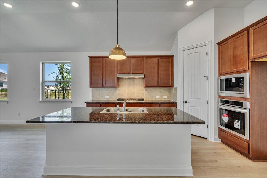 Kitchen with tasteful backsplash, dark stone counters, brown cabinetry, recessed lighting, and stainless steel appliances Kitchen with tasteful backsplash, dark stone counters, brown cabinetry, recessed lighting, and stainless steel appliances