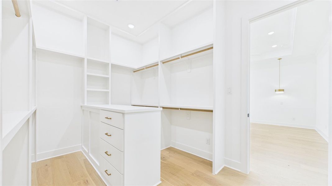 Spacious walk-in closet with ample shelving and hanging space, featuring a central drawer unit. Bright, white finish and recessed lighting create a clean, modern look.