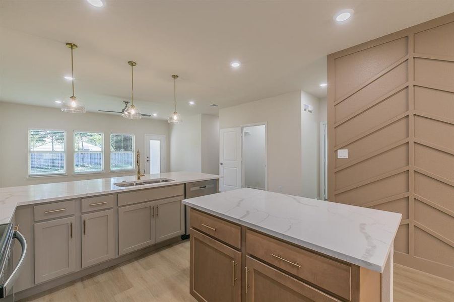 Kitchen featuring pendant lighting, sink, light hardwood / wood-style flooring, light stone countertops, and a kitchen island