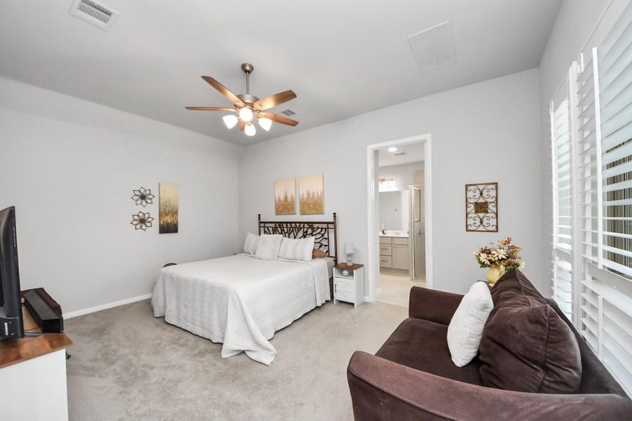 The large primary bedroom features neutral tones, a ceiling fan and plush carpeting. It has an en-suite bathroom and large windows with shutters, providing ample natural light. The large primary bedroom features neutral tones, a ceiling fan and plush carpeting. It has an en-suite bathroom and large windows with shutters, providing ample natural light.