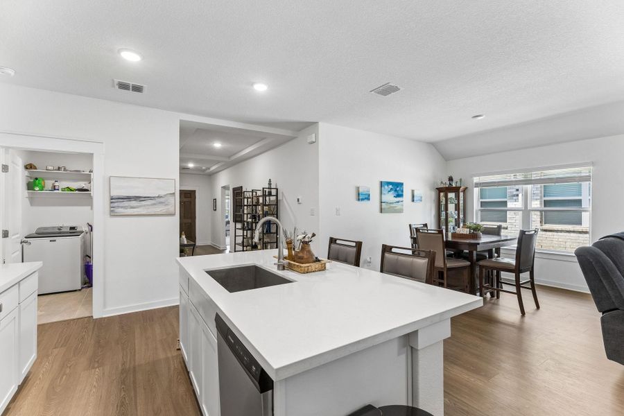 Kitchen island with a stainless steel sink and integrated dishwasher, wood-finish flooring, recessed lighting, and an adjacent dining area with a large window