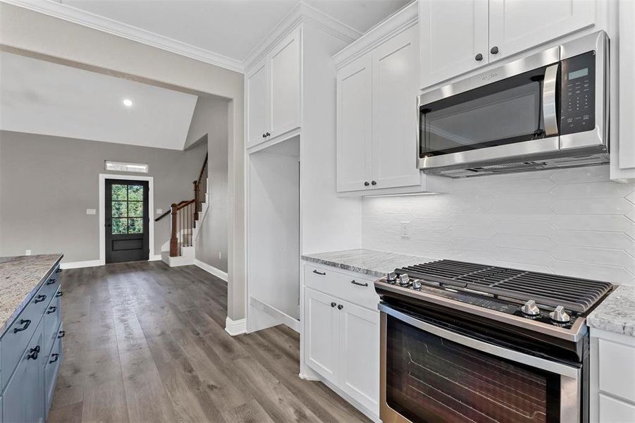 Kitchen featuring light stone countertops, appliances with stainless steel finishes, white cabinetry, decorative backsplash, and light hardwood / wood-style flooring