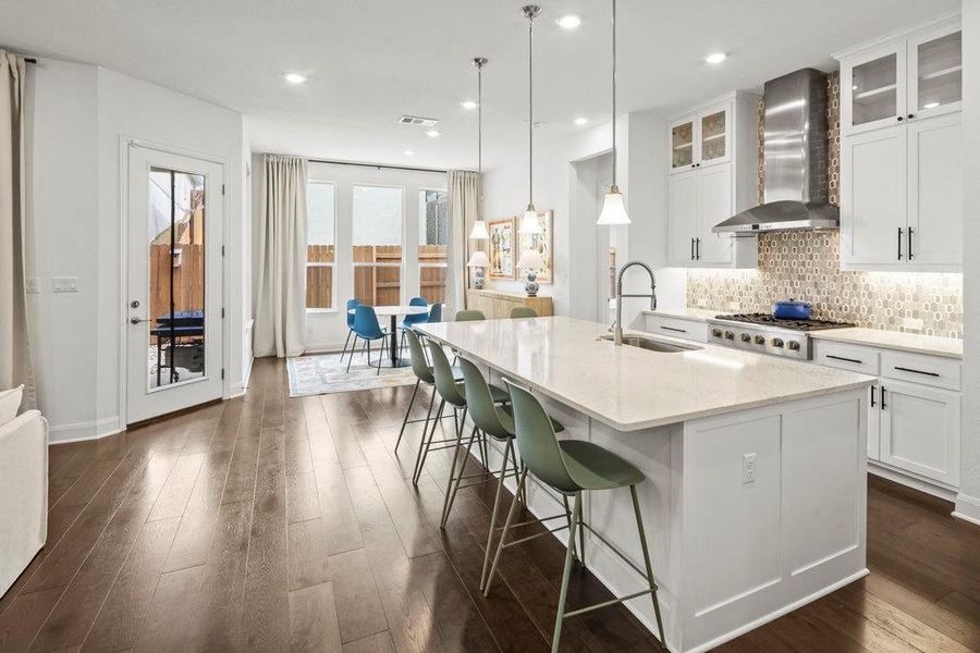 Kitchen featuring a kitchen island with sink, a sink, tasteful backsplash, gas stovetop, and wall chimney exhaust hood