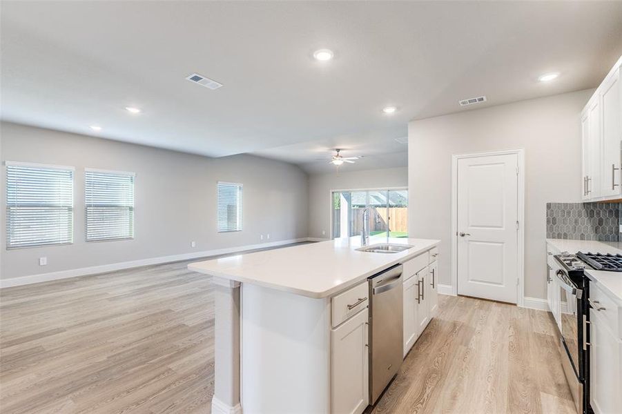Kitchen featuring open floor plan, light wood-style flooring, white cabinetry, decorative backsplash, and black range with gas cooktop Kitchen featuring open floor plan, light wood-style flooring, white cabinetry, decorative backsplash, and black range with gas cooktop