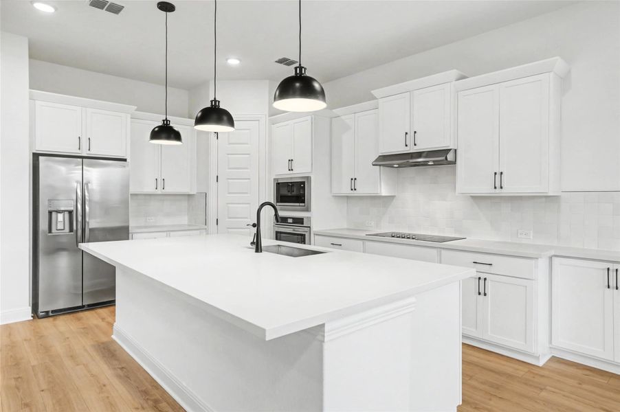 Kitchen with stainless steel appliances, white cabinets, a center island with sink, and light wood-type flooring