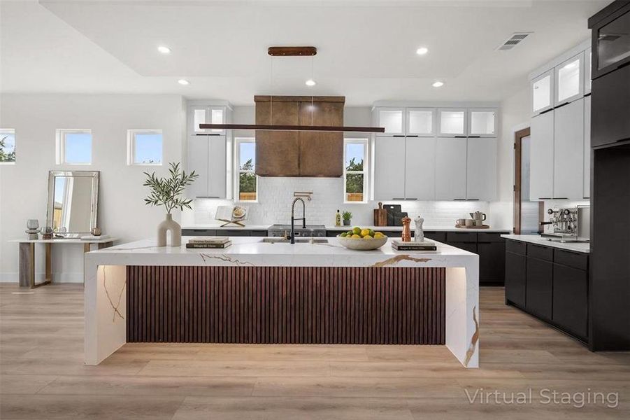 The kitchen features a large island with a fluted wood base and a waterfall countertop, light wood flooring, and recessed lighting The kitchen features a large island with a fluted wood base and a waterfall countertop, light wood flooring, and recessed lighting