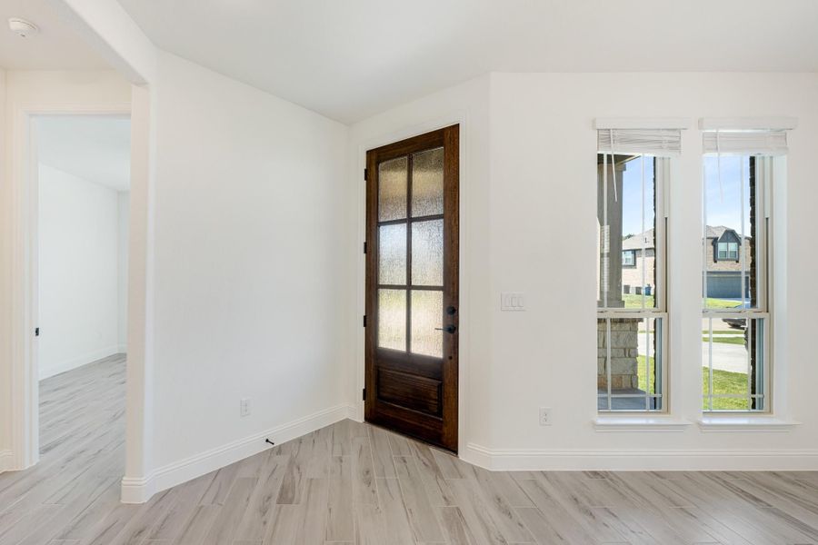 Entryway with dark wood glass-panel door, light gray wood floors, and white walls with double windows Entryway with dark wood glass-panel door, light gray wood floors, and white walls with double windows