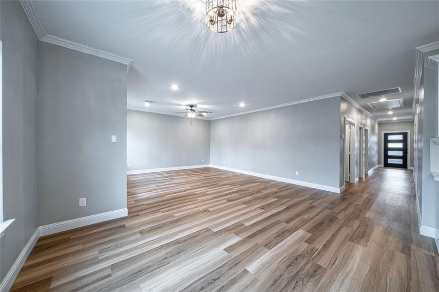 Empty room featuring light hardwood / wood-style floors, crown molding, and ceiling fan with notable chandelier