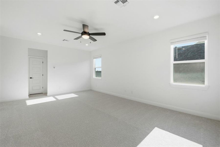 Spacious room featuring light gray carpeting, crisp white walls, a multi-paneled door with dark hardware, recessed lighting, and a ceiling fan with integrated illumination
