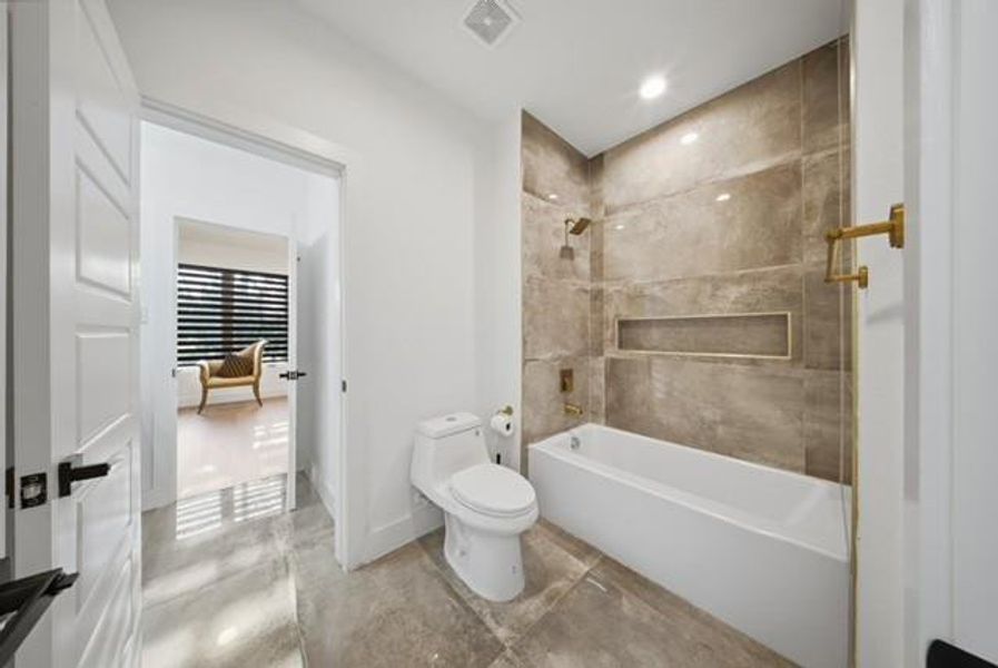 Full bath with a white bathtub, integrated shower niche, gold-tone fixtures, and large format tile flooring