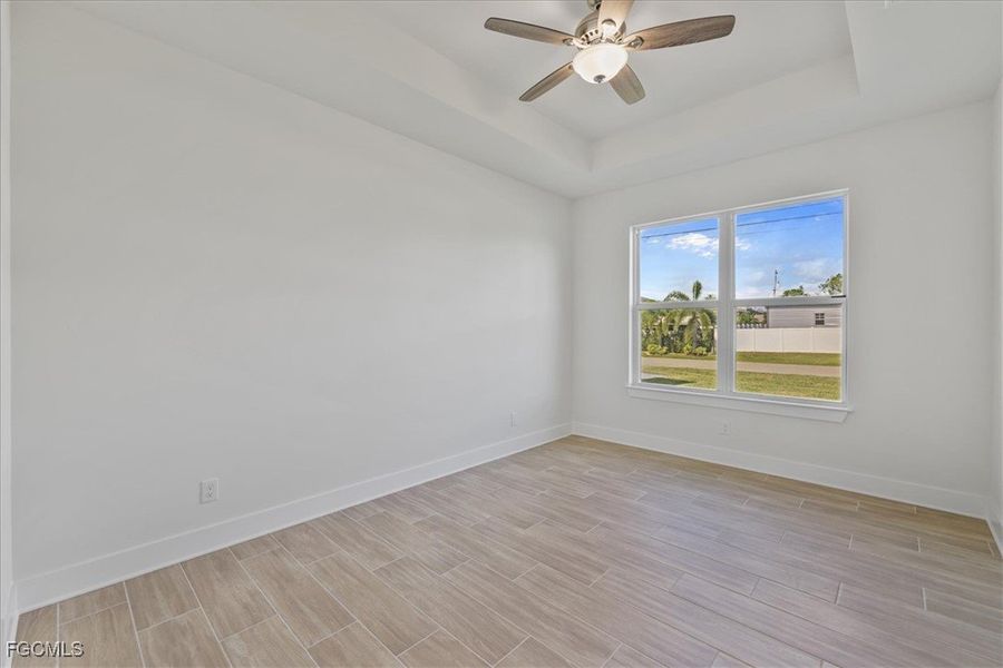 Empty room featuring wood finish floors, a tray ceiling, and a ceiling fan