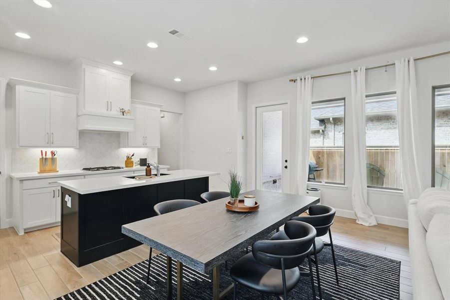 Kitchen with visible vents, backsplash, a sink, light wood-type flooring, and a kitchen island with sink