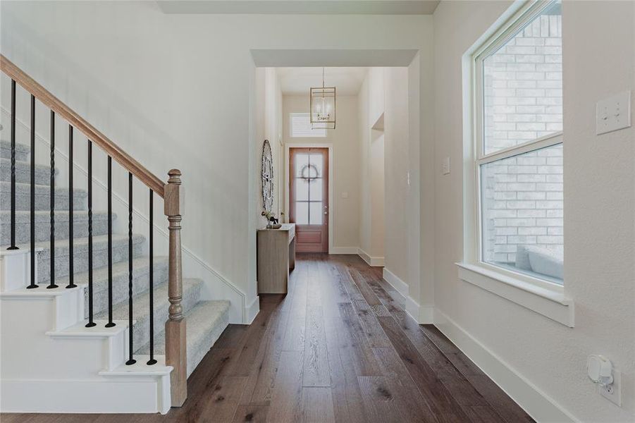Entryway featuring rich wood-finish flooring, a carpeted staircase with wood handrails and black iron balusters, and a front door with frosted glass