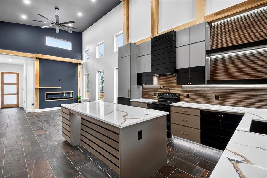 Two tone kitchen featuring a center island, two tone cabinetry, a high ceiling, black electric range oven, and light stone countertops Two tone kitchen featuring a center island, two tone cabinetry, a high ceiling, black electric range oven, and light stone countertops