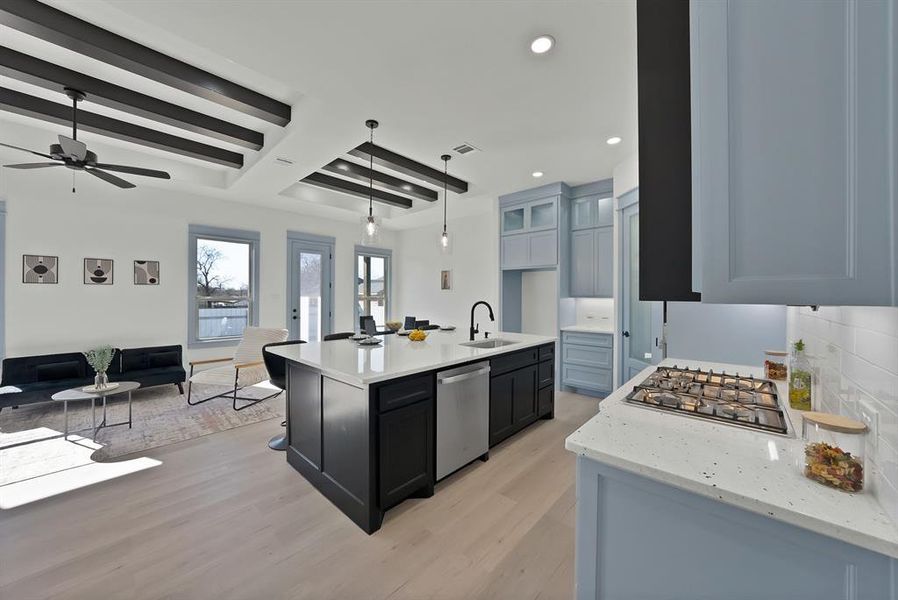 Kitchen featuring beamed ceiling, open floor plan, a kitchen island with sink, light stone countertops, and light wood-style floors